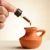 Pipetje met een druppel CBD-olie 16,73% die in een klein terracotta kruikje valt