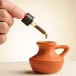 Pipetje met een druppel CBD-olie 16,73% die in een klein terracotta kruikje valt