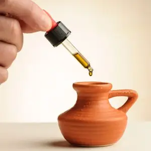 Pipetje met een druppel CBD-olie 5,65% die in een klein terracotta kruikje valt