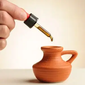 Pipetje met een druppel CBD-olie 8,77% die in een klein terracotta kruikje valt