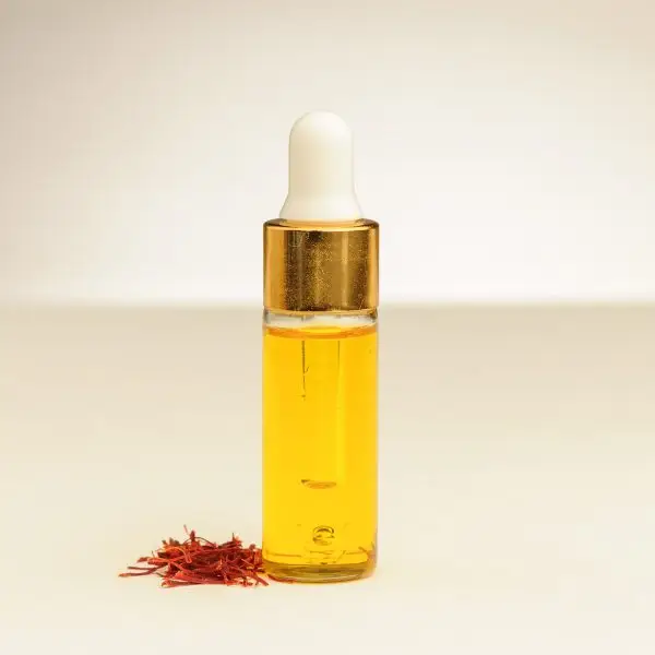 Een 4 ml flesje etherische saffraanolie met saffraan draden ernaast.aromatische verwennerij