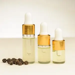 Drie flesjes zwarte peper etherische olie (3 ml, 3 ml en 4 ml) naast zwarte peperkorrels