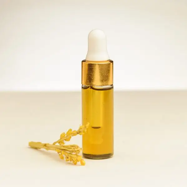 4 ml flesje etherische mimosa-olie naast een mimosa bloesem